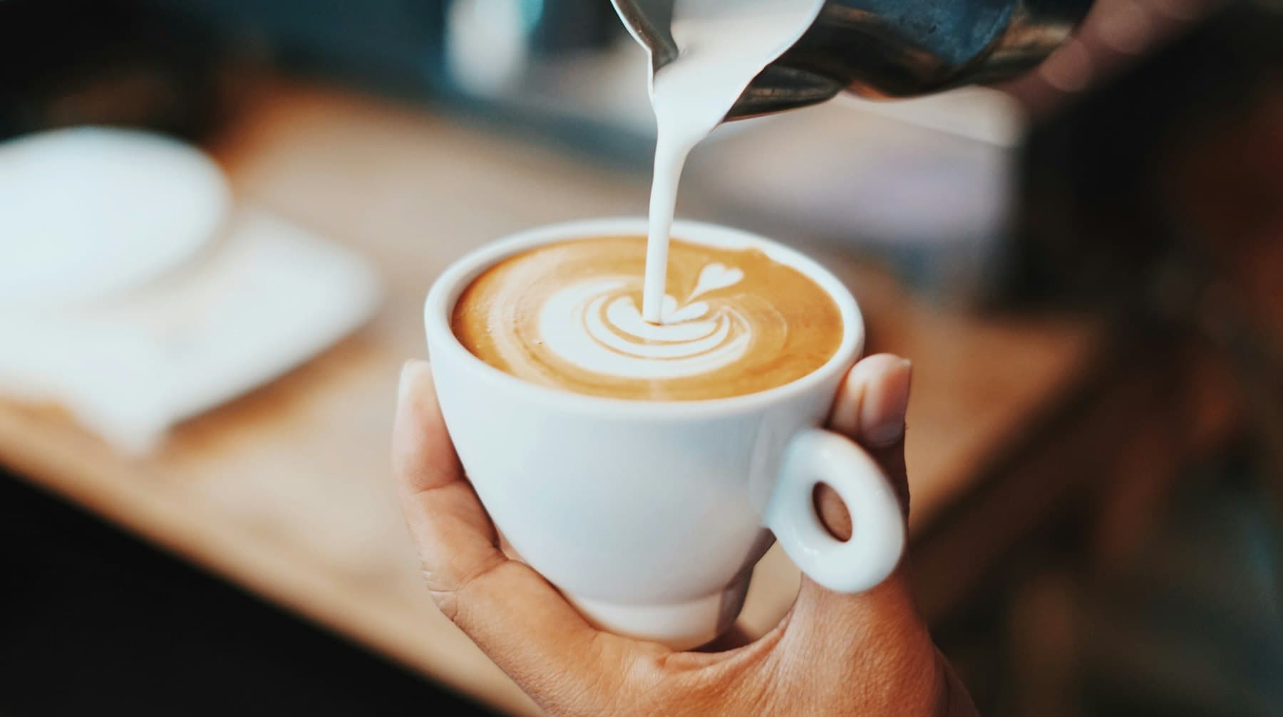 Barista pouring steamed milk into a latte, drawing a heart