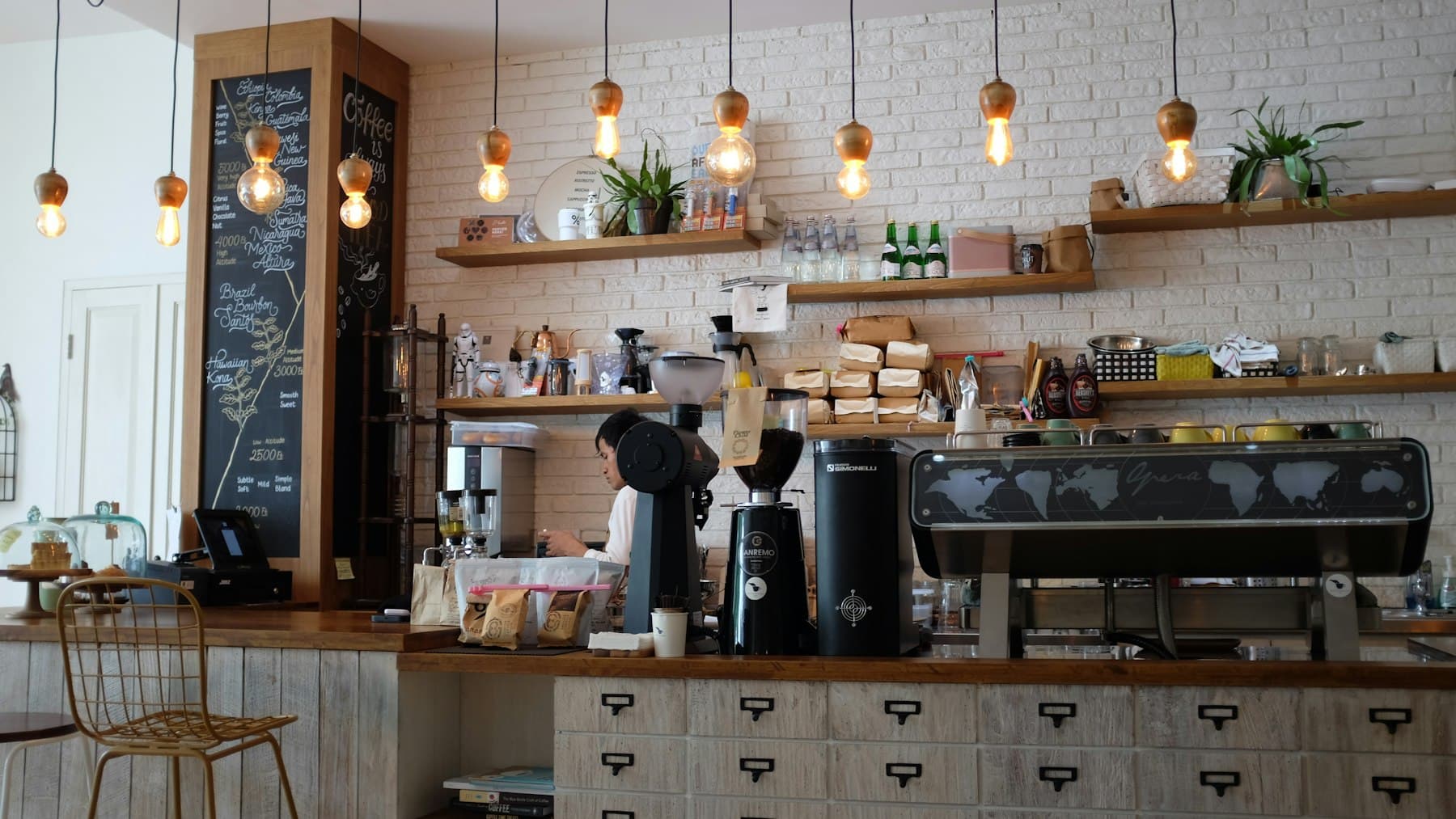 Warm café counter with hanging bulbs and a barista at work